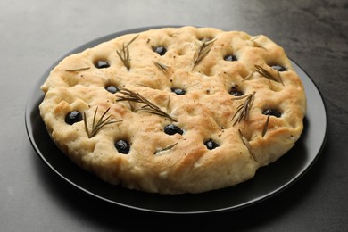 Photo of Delicious focaccia bread with olives and rosemary on grey table, closeup