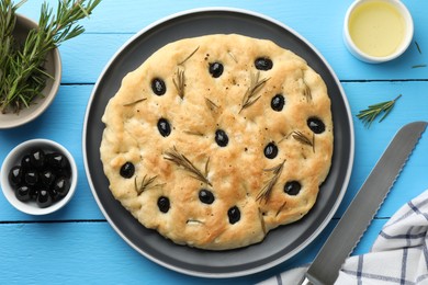 Photo of Delicious focaccia bread with olives, rosemary and oil on light blue wooden table, flat lay