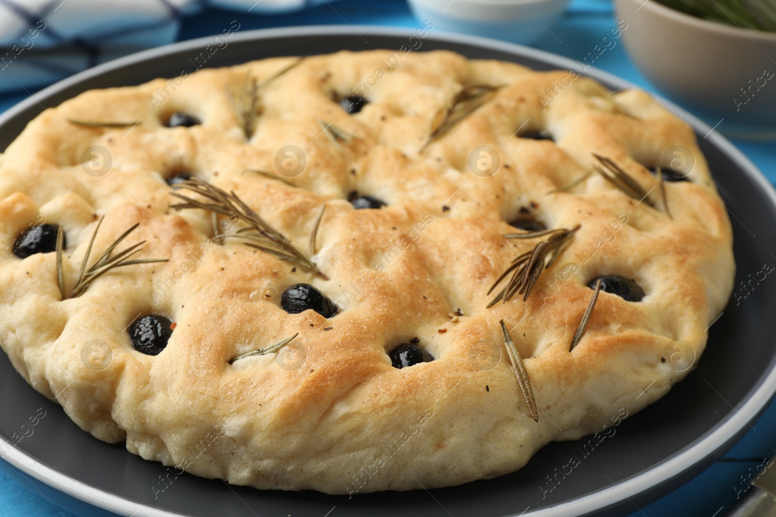 Photo of Delicious focaccia bread with olives and rosemary on table, closeup