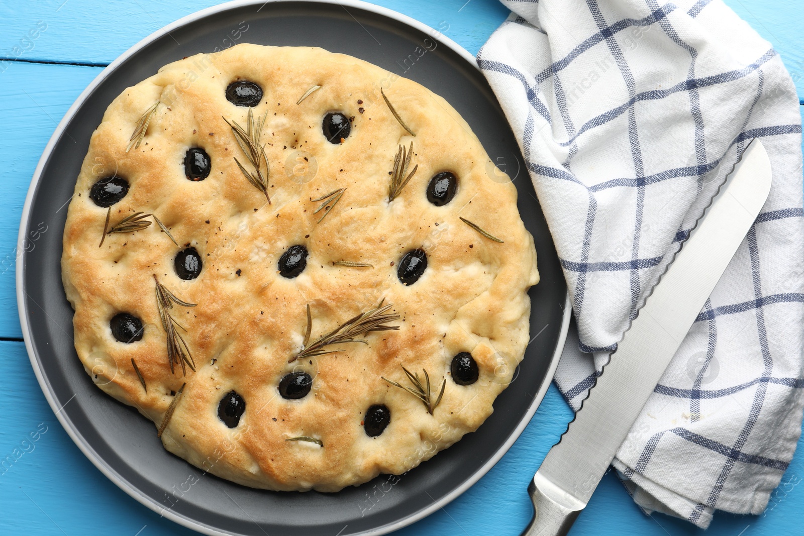 Photo of Delicious focaccia bread with olives, rosemary and knife on light blue wooden table, top view