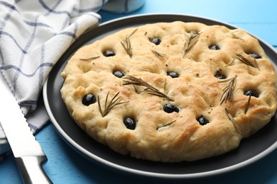 Photo of Delicious focaccia bread with olives, rosemary and knife on light blue wooden table, closeup