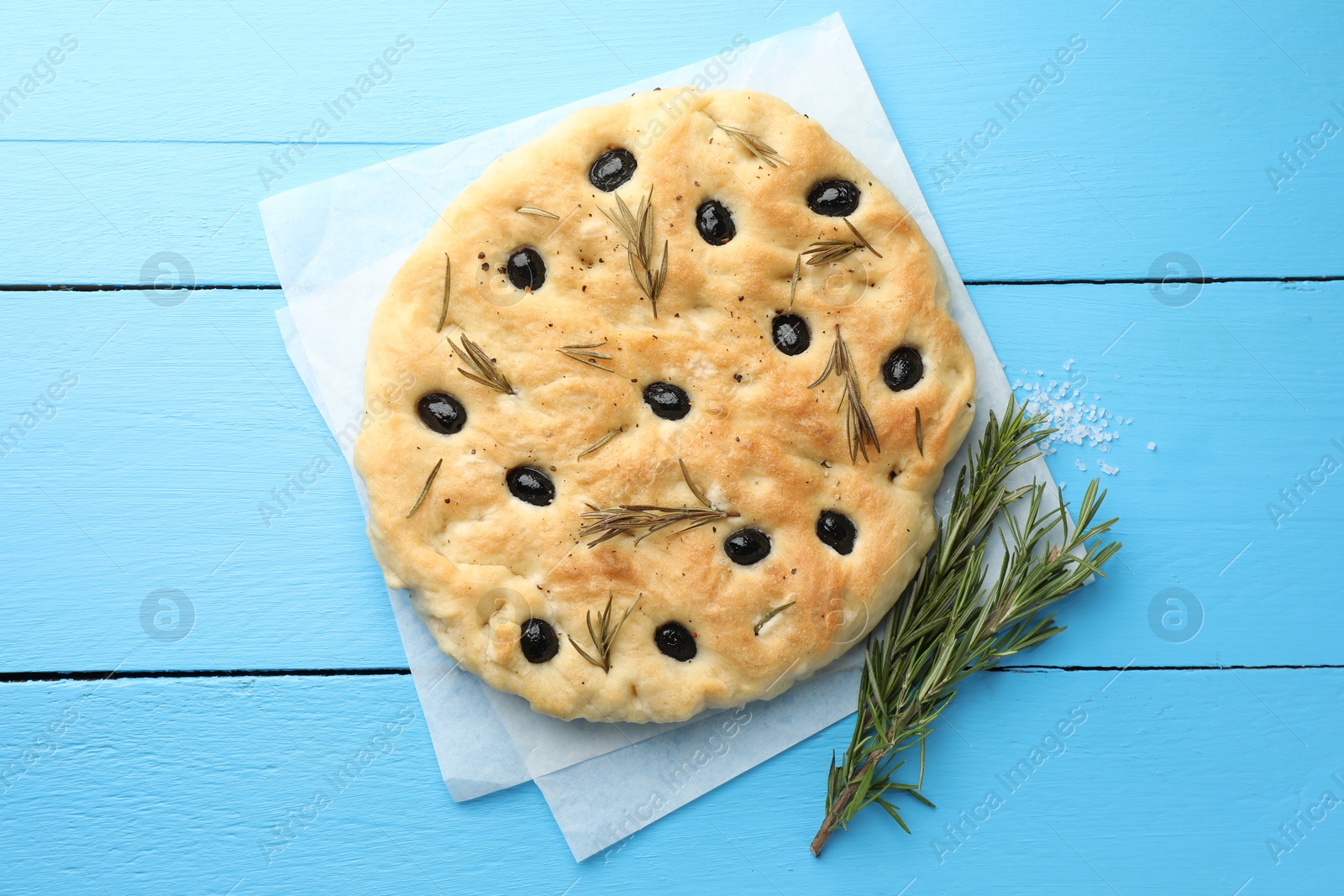 Photo of Delicious focaccia bread with olives, rosemary and salt on light blue wooden table, top view