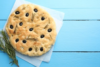 Photo of Delicious focaccia bread with olives, rosemary and salt on light blue wooden table, top view. Space for text