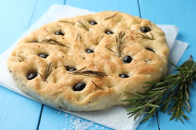 Photo of Delicious focaccia bread with olives, rosemary and salt on light blue wooden table, closeup