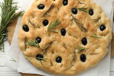 Photo of Delicious focaccia bread with olives and rosemary on white wooden table, top view