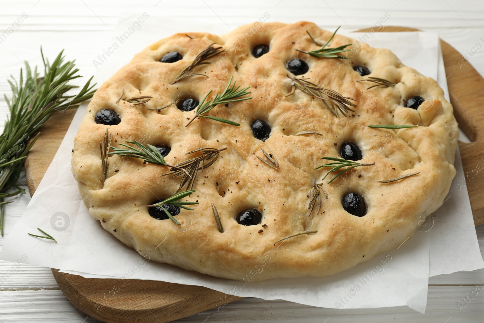 Photo of Delicious focaccia bread with olives and rosemary on white wooden table, closeup