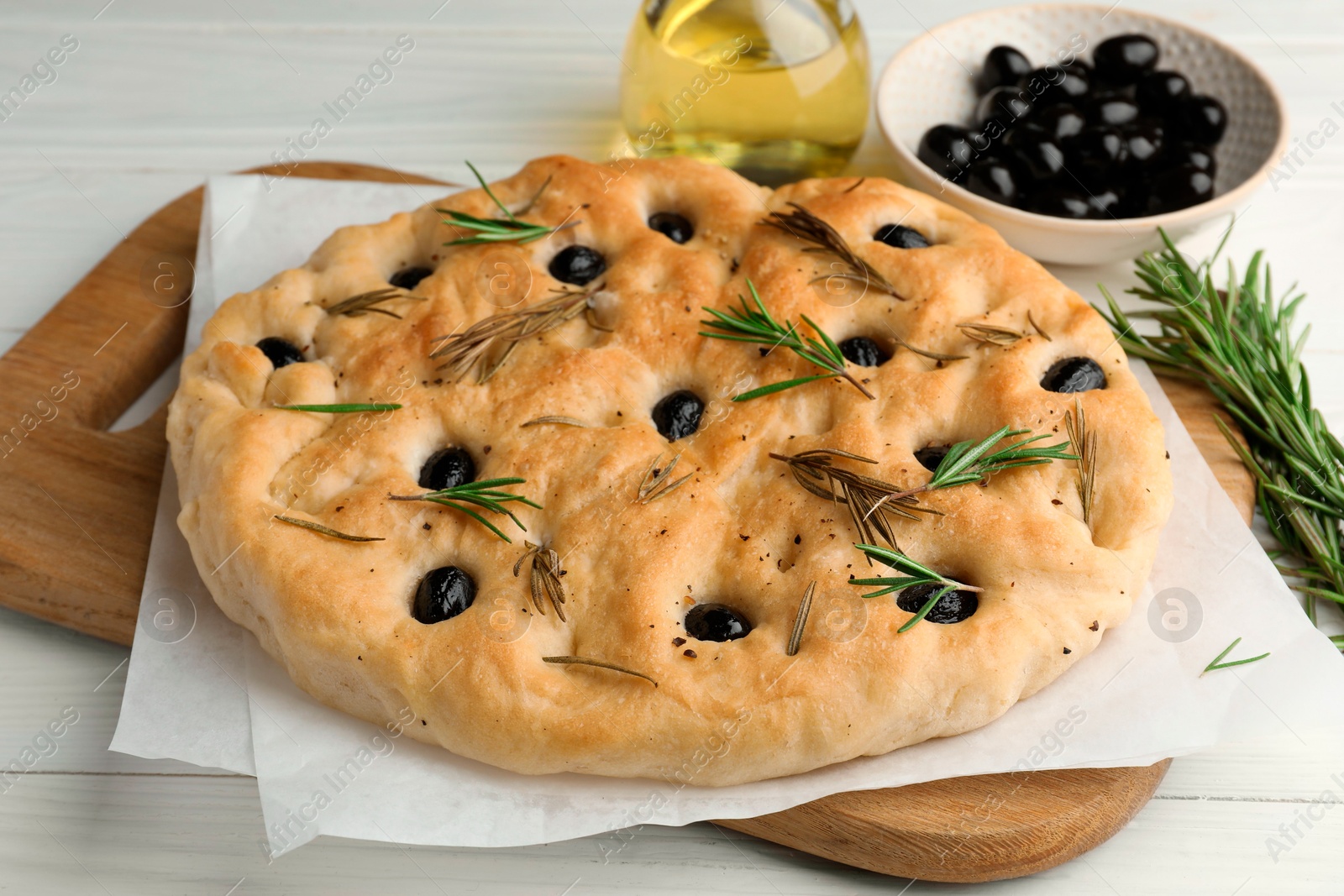 Photo of Delicious focaccia bread with olives, rosemary and oil on white wooden table, closeup