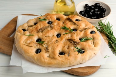 Photo of Delicious focaccia bread with olives, rosemary and oil on white wooden table, closeup