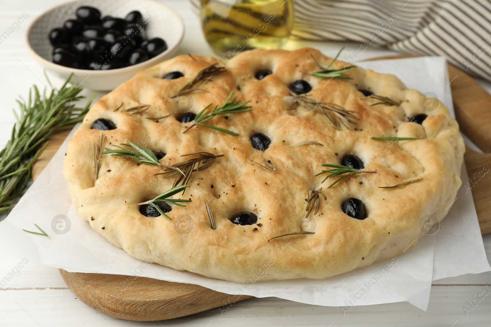 Photo of Delicious focaccia bread with olives and rosemary on white wooden table, closeup