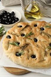 Photo of Delicious focaccia bread with olives, rosemary and oil on white table, closeup