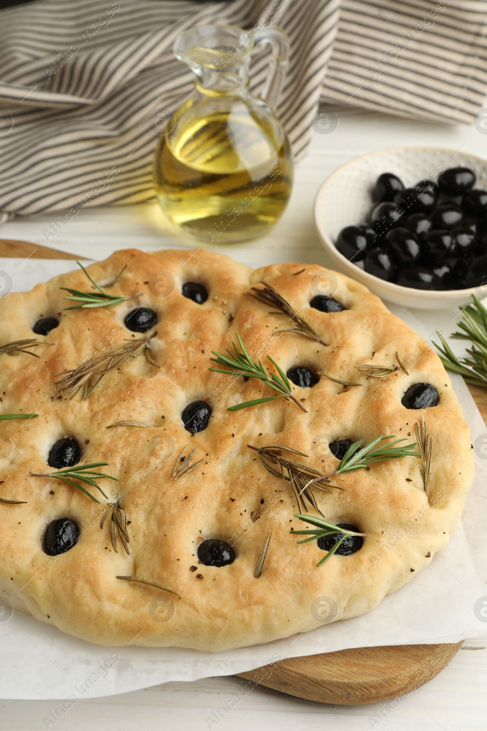 Photo of Delicious focaccia bread with olives, rosemary and oil on white table, closeup