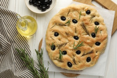 Photo of Delicious focaccia bread with olives, rosemary and oil on white wooden table, flat lay