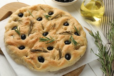 Photo of Delicious focaccia bread with olives, rosemary and oil on white wooden table, closeup