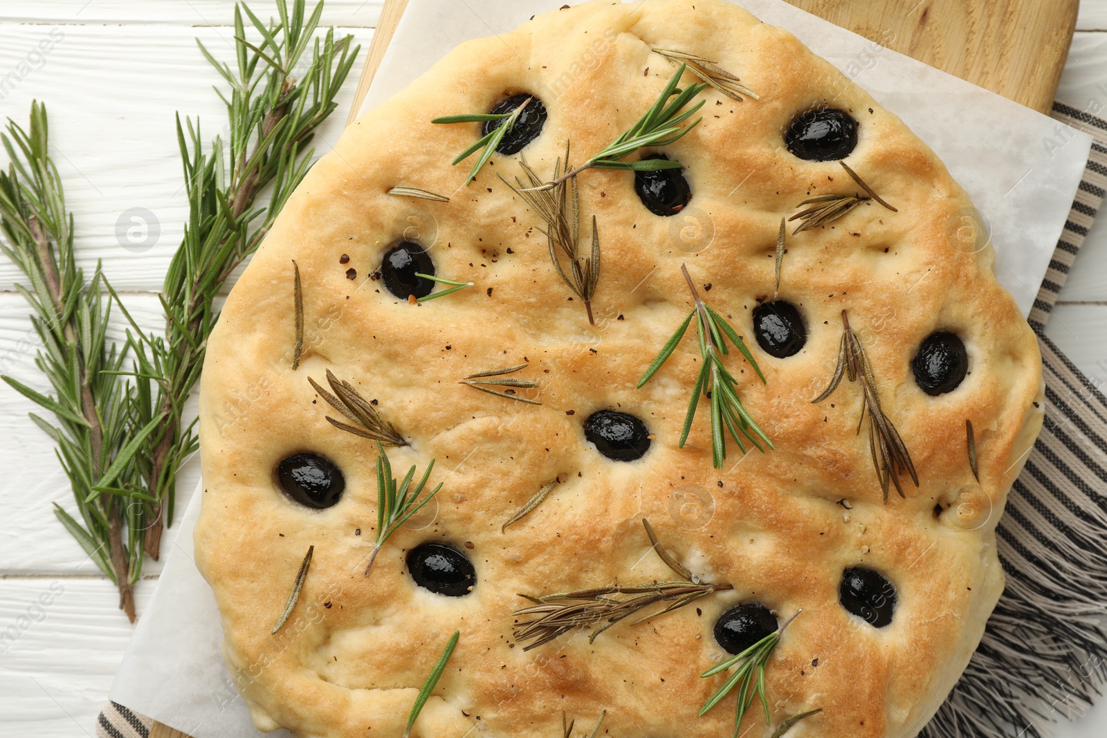 Photo of Delicious focaccia bread with olives and rosemary on white wooden table, top view