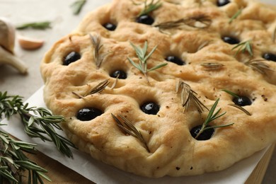 Photo of Delicious focaccia bread with olives, rosemary and garlic on table, closeup