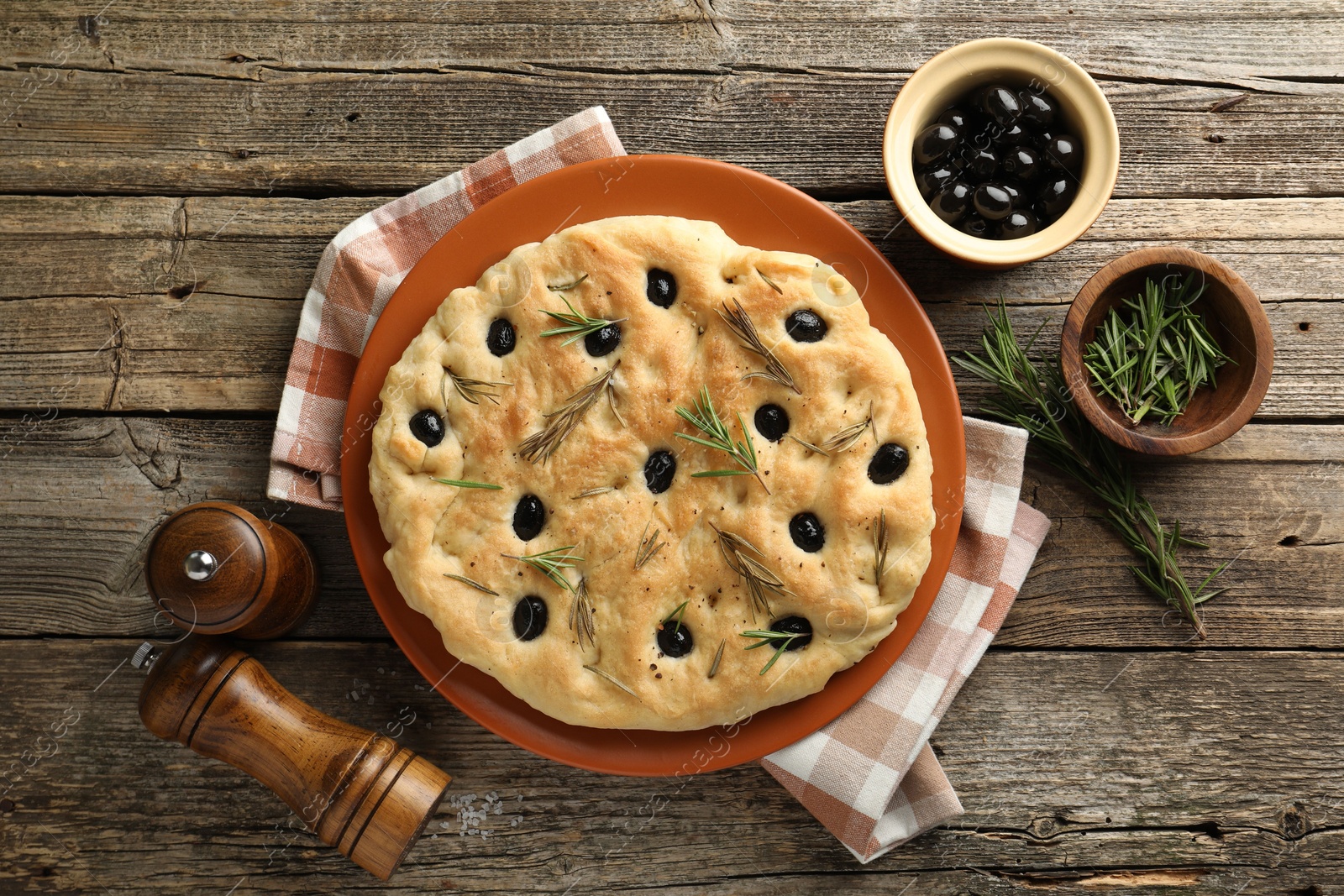 Photo of Delicious focaccia bread with olives, rosemary and spices on wooden table, flat lay