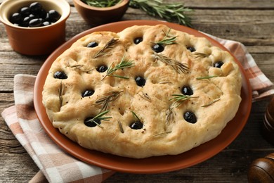 Photo of Delicious focaccia bread with olives and rosemary on wooden table, closeup