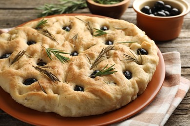 Photo of Delicious focaccia bread with olives and rosemary on wooden table, closeup