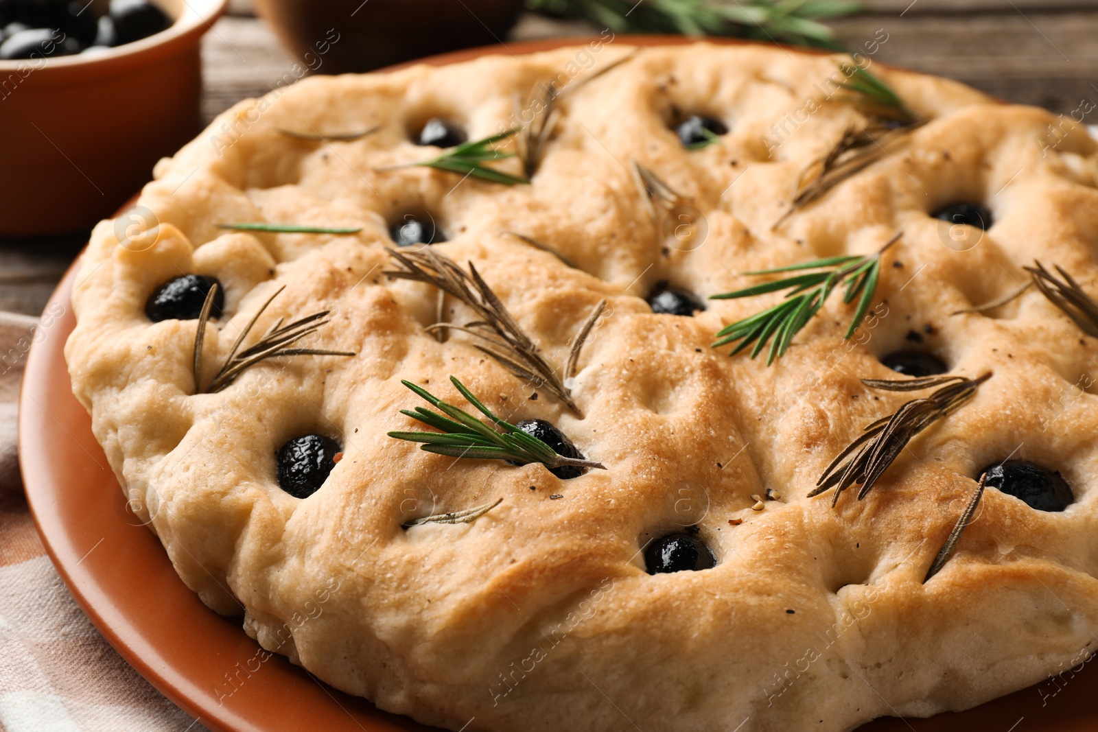 Photo of Delicious focaccia bread with olives and rosemary on table, closeup