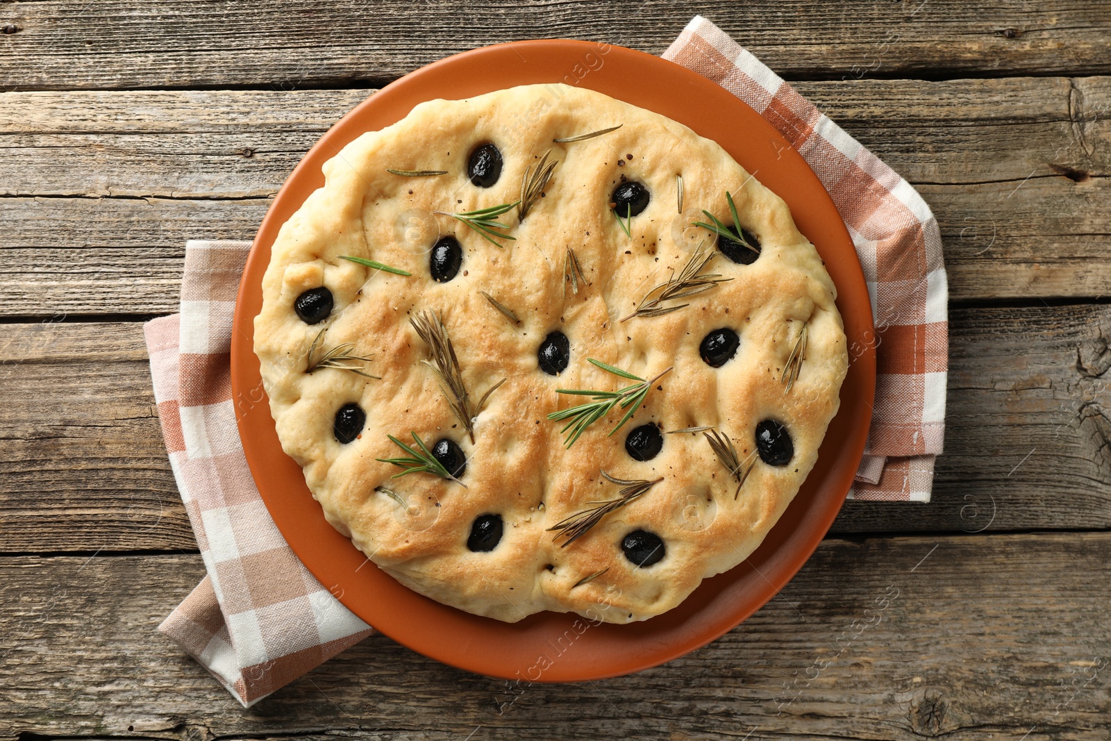 Photo of Delicious focaccia bread with olives and rosemary on wooden table, top view