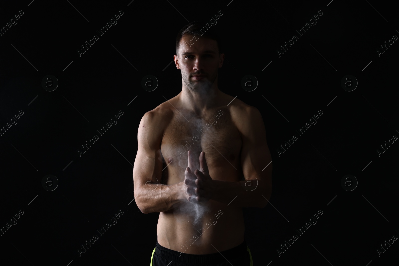 Photo of Man clapping hands with talcum powder before training on black background