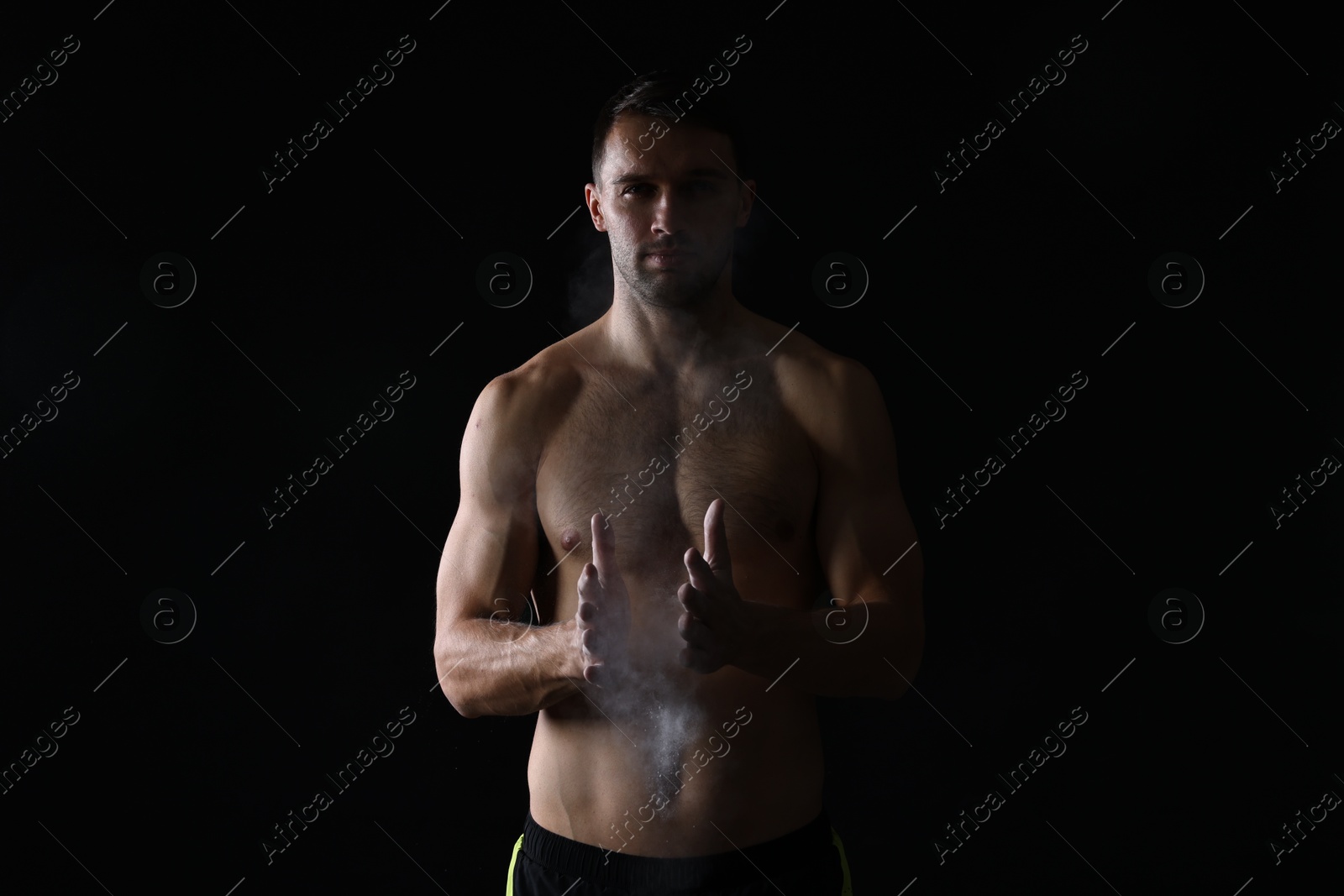 Photo of Man clapping hands with talcum powder before training on black background