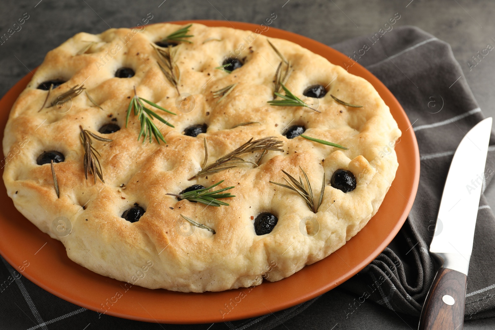 Photo of Delicious focaccia bread with olives, rosemary and knife on grey table, closeup