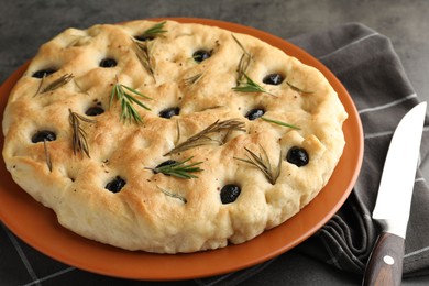 Photo of Delicious focaccia bread with olives, rosemary and knife on grey table, closeup