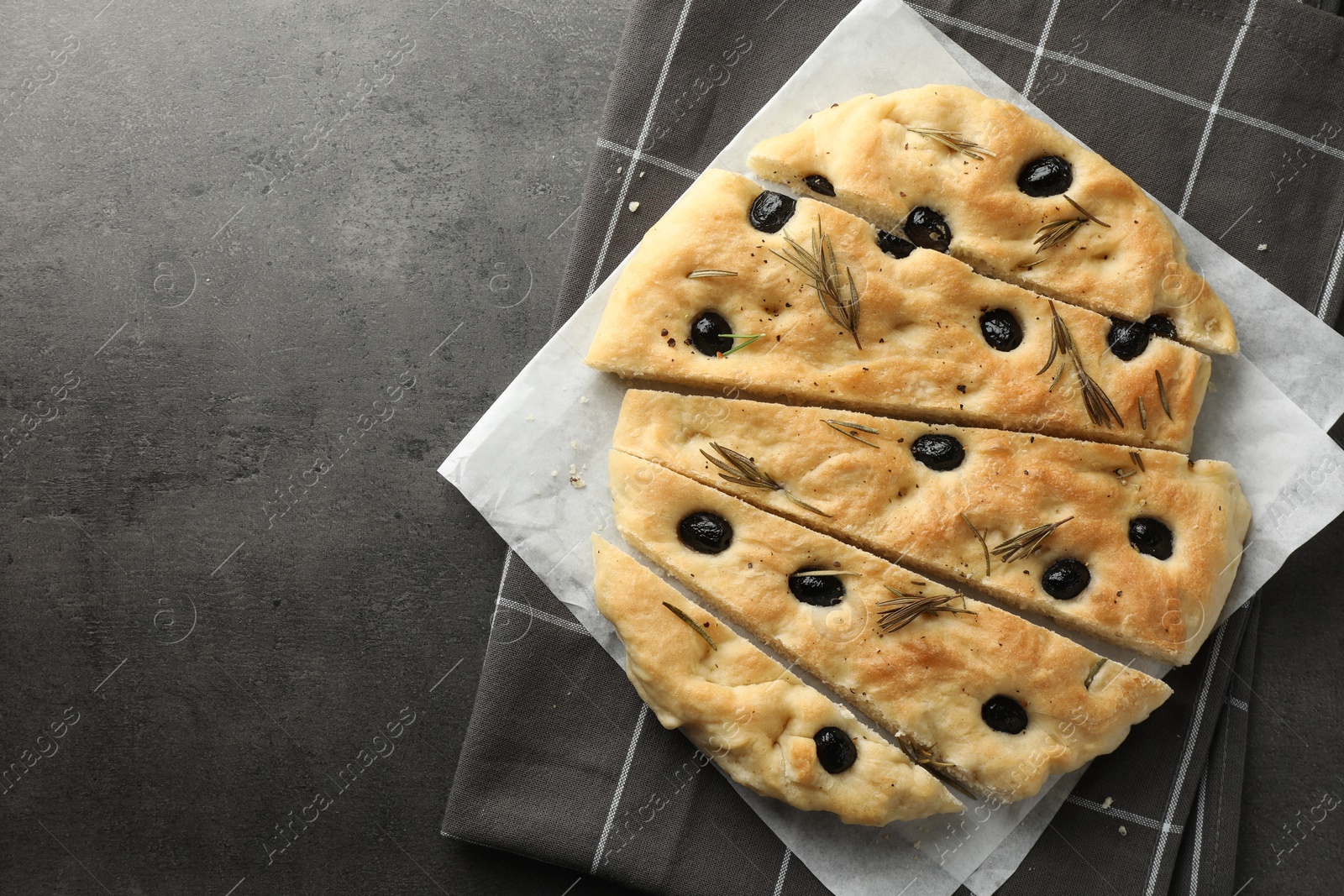 Photo of Slices of delicious focaccia bread with olives and rosemary on grey table, top view. Space for text