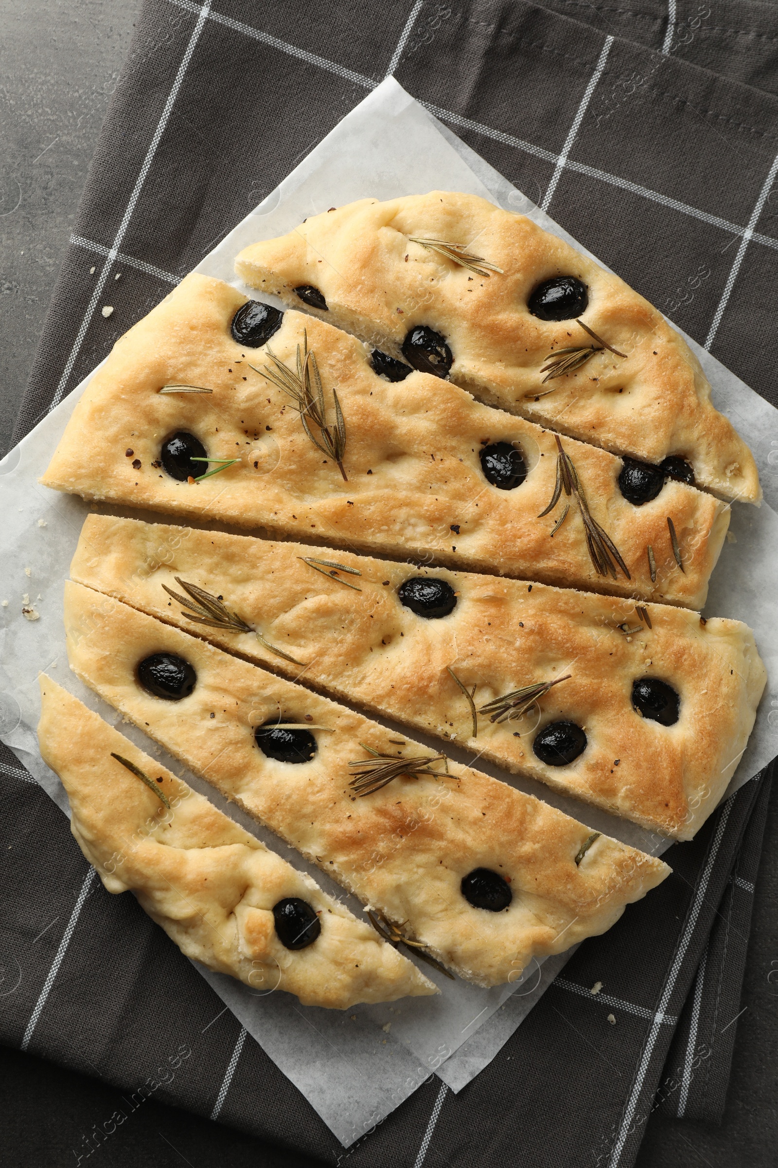 Photo of Slices of delicious focaccia bread with olives and rosemary on grey table, top view