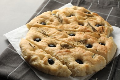 Photo of Slices of delicious focaccia bread with olives and rosemary on grey table, closeup