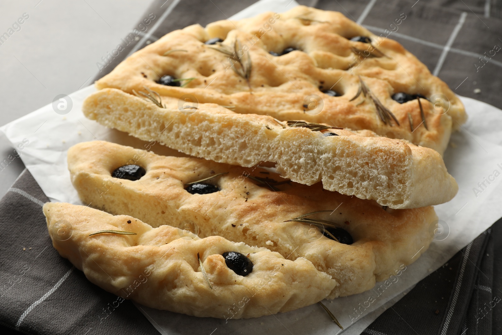 Photo of Slices of delicious focaccia bread with olives and rosemary on grey table, closeup