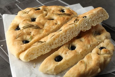 Photo of Slices of delicious focaccia bread with olives and rosemary on table, closeup