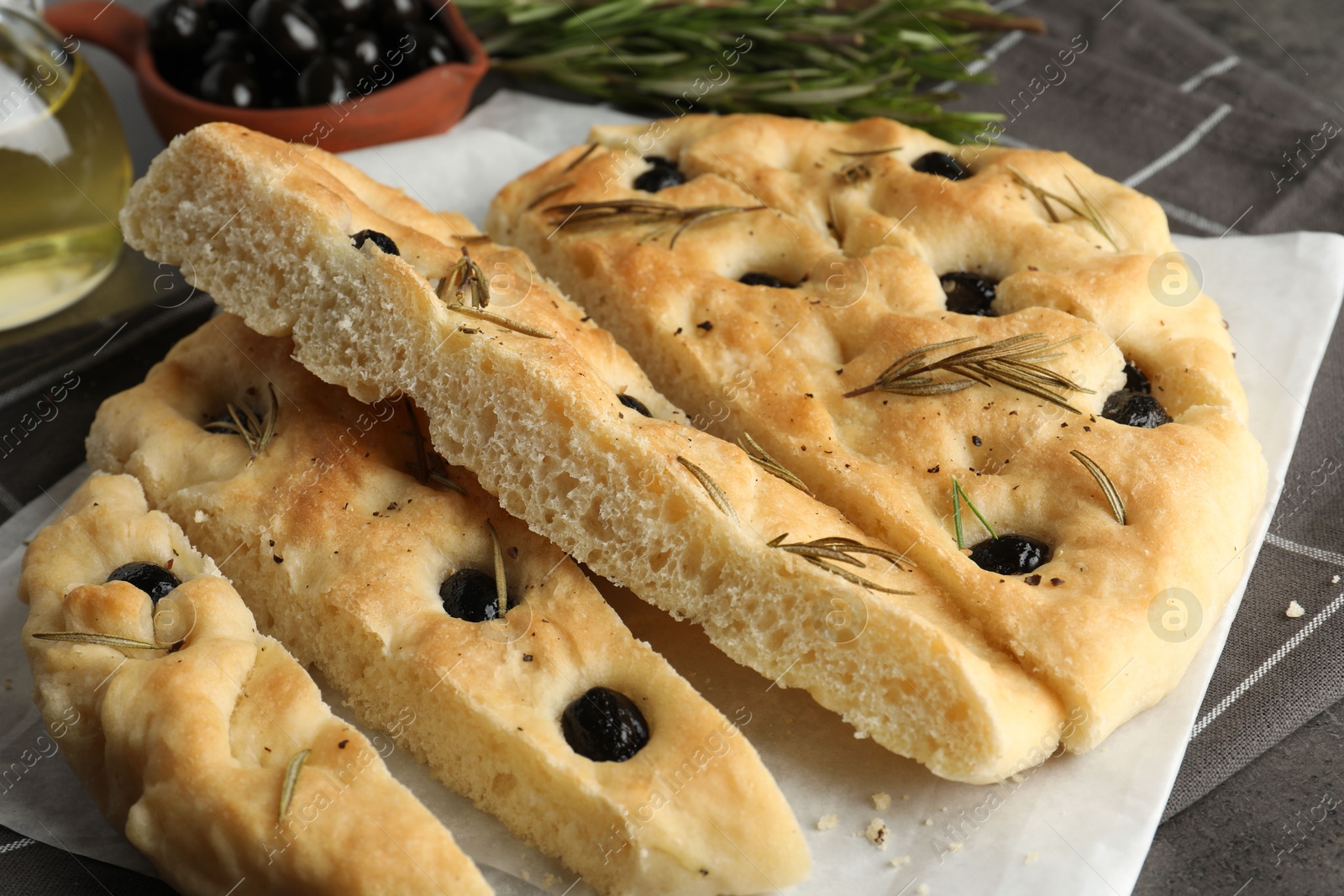 Photo of Slices of delicious focaccia bread with olives and rosemary on table, closeup