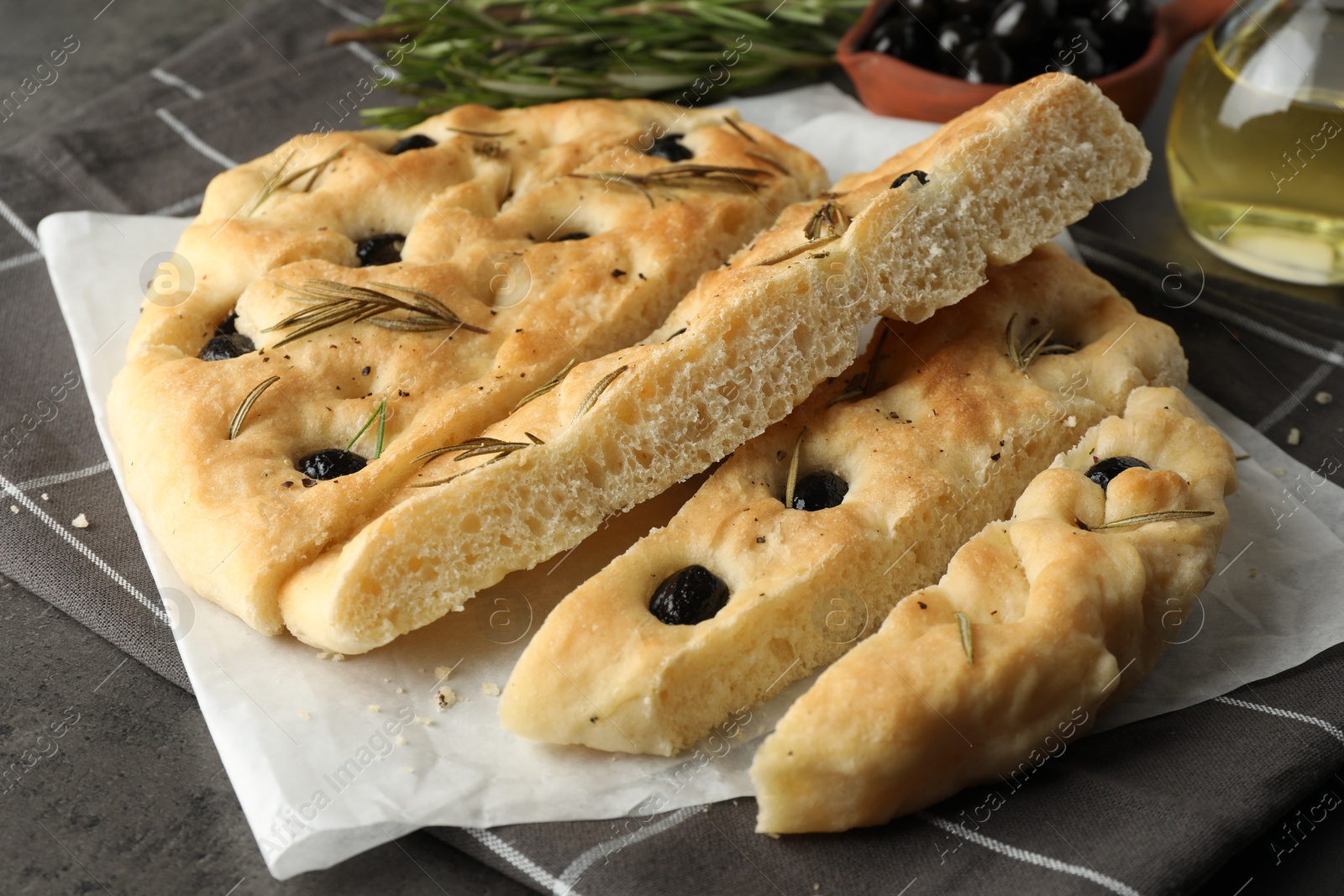 Photo of Slices of delicious focaccia bread with olives and rosemary on table, closeup