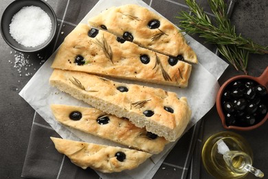 Photo of Slices of delicious focaccia bread with olives, rosemary, oil and salt on grey table, flat lay