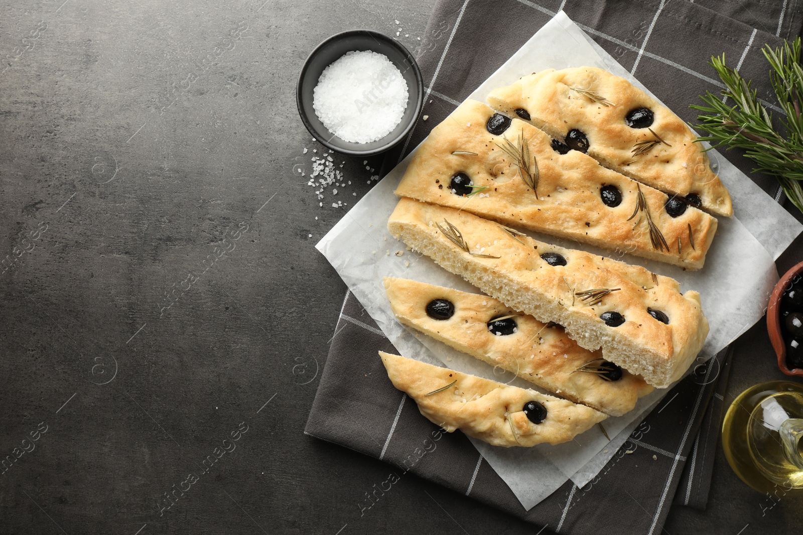 Photo of Slices of delicious focaccia bread with olives, rosemary and spices on grey table, flat lay. Space for text