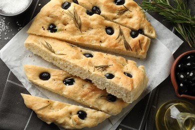 Photo of Slices of delicious focaccia bread with olives, rosemary, oil and salt on grey table, flat lay