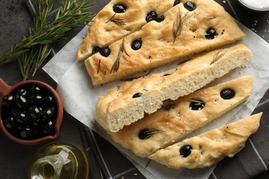 Photo of Slices of delicious focaccia bread with olives, rosemary, oil and salt on grey table, flat lay