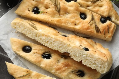 Photo of Slices of delicious focaccia bread with olives, rosemary and salt on table, flat lay