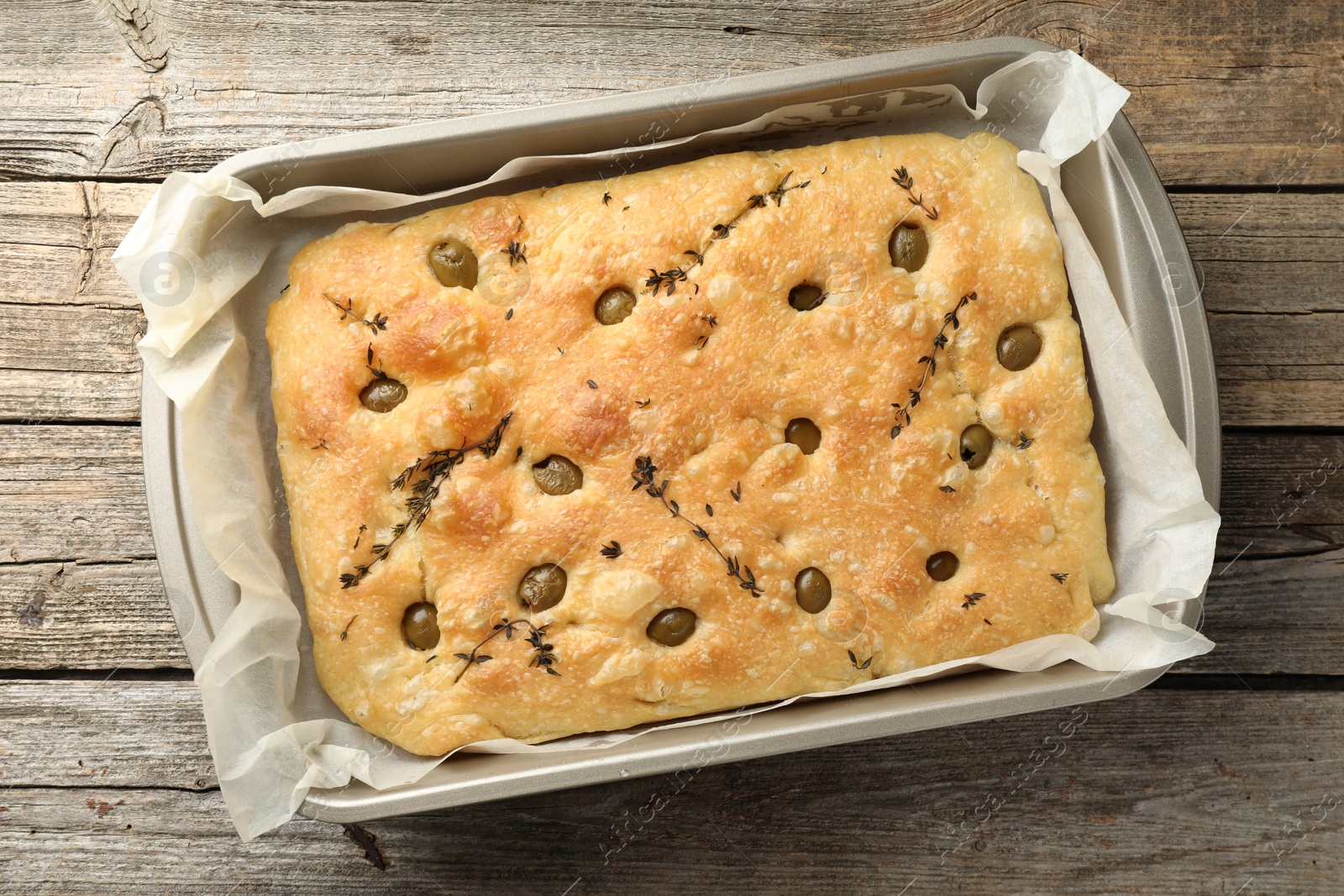 Photo of delicious focaccia bread with olives and thyme in baking dish on wooden table, top view