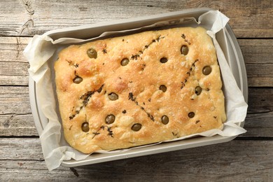 Photo of delicious focaccia bread with olives and thyme in baking dish on wooden table, top view