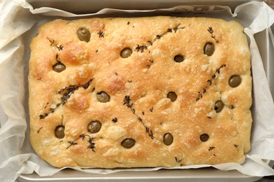 Photo of Delicious focaccia bread with olives and thyme in baking dish on table, top view