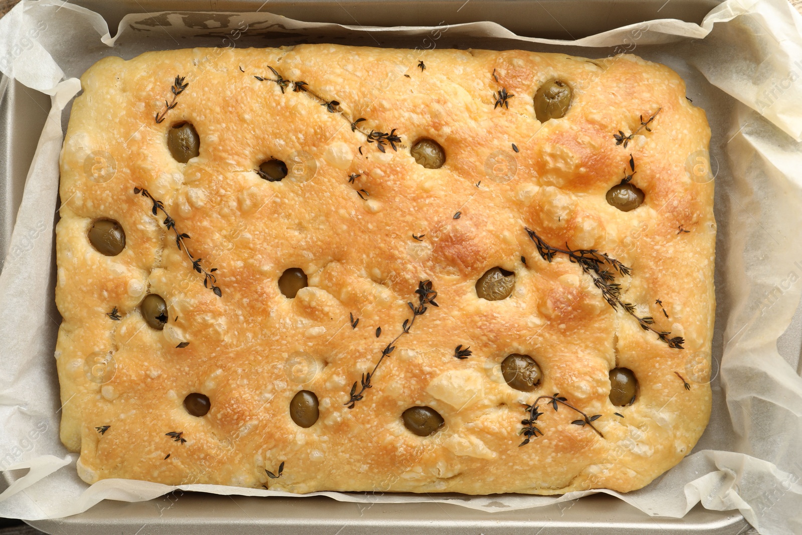 Photo of Delicious focaccia bread with olives and thyme in baking dish on table, top view