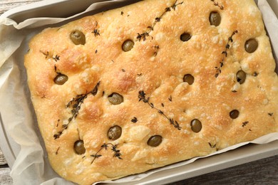 Photo of Delicious focaccia bread with olives and thyme in baking dish on wooden table, top view