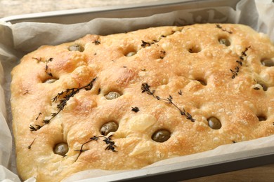 Photo of Delicious focaccia bread with olives and thyme in baking dish on table, closeup