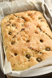 Photo of Delicious focaccia bread with olives and thyme in baking dish on table, closeup