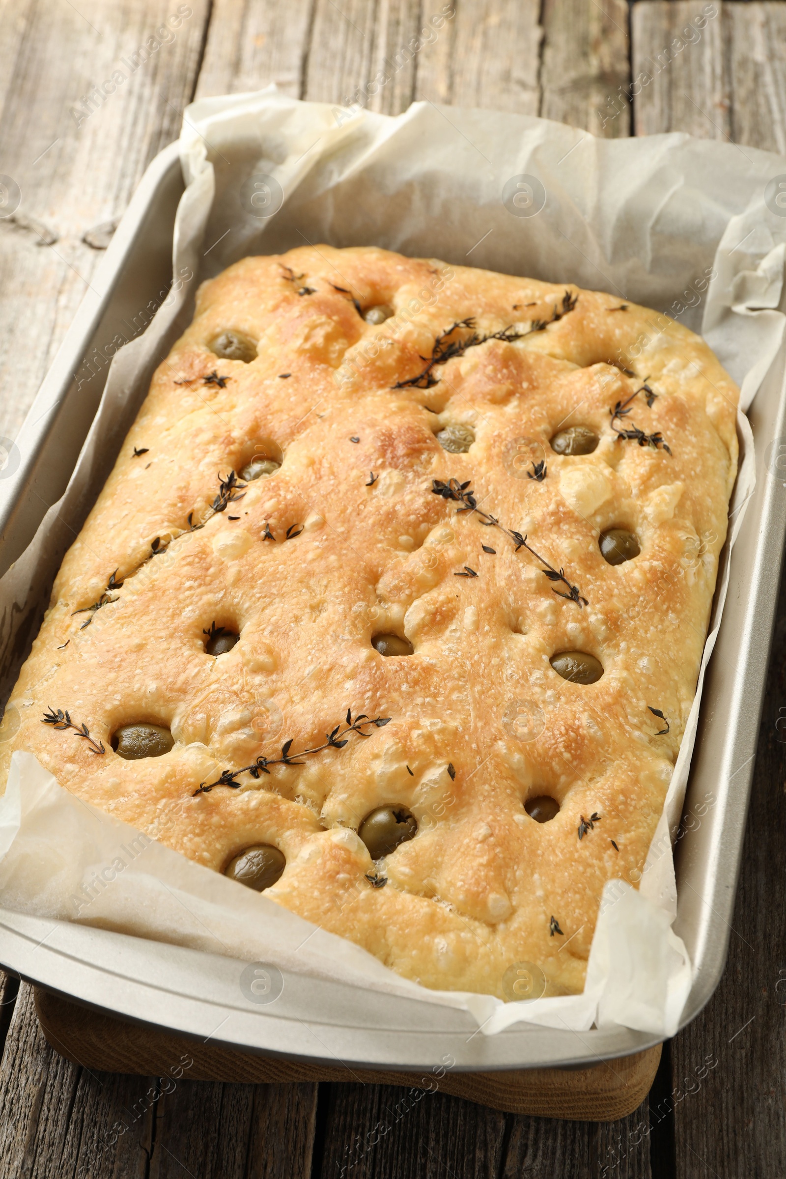 Photo of Delicious focaccia bread with olives and thyme in baking dish on wooden table, closeup