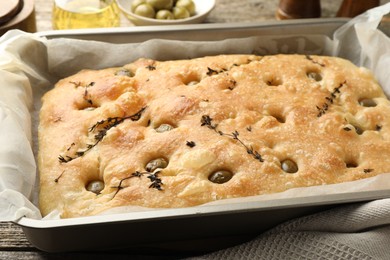 Photo of Delicious focaccia bread with olives and thyme in baking dish on table, closeup