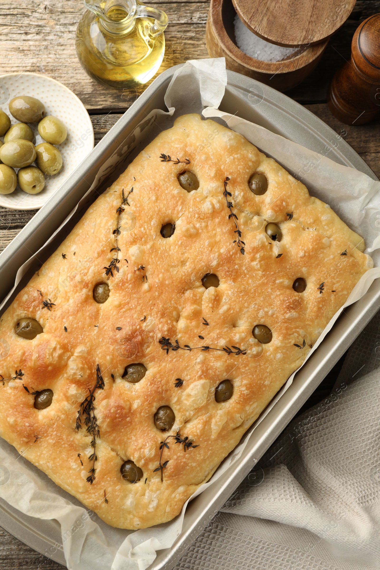 Photo of Delicious focaccia bread with olives, thyme, salt and oil on wooden table, flat lay